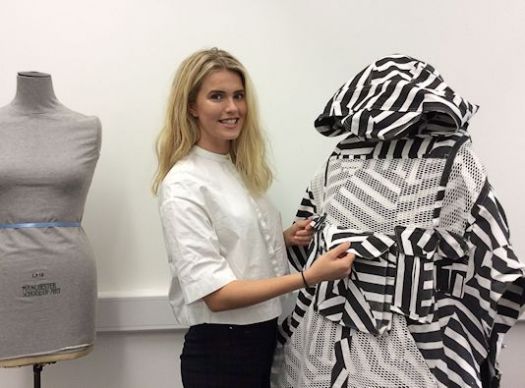 A female student, Hannah, poses with one of her black and white geometric designs